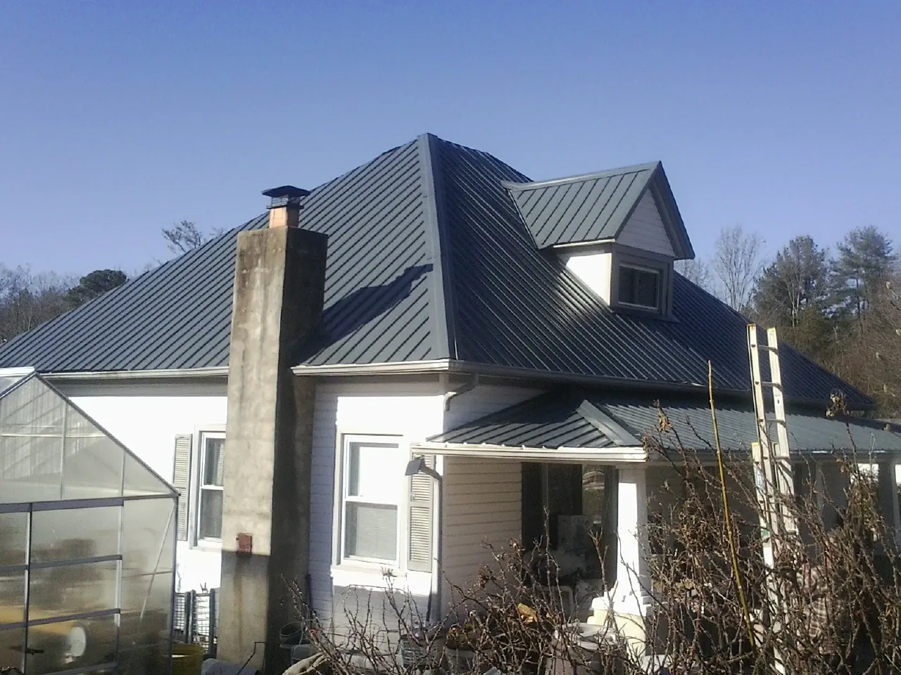 Dark blue standing seam metal roof on a white farmhouse with dormer — Slate & Tile Roof Repair by Roofing Brothers in Willow Spring