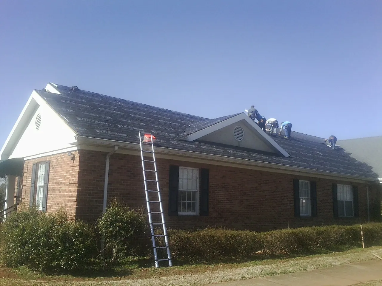 Crew tearing shingles off a brick ranch roof with a ladder set — Emergency Roof Repair work by our crew in Willow Spring