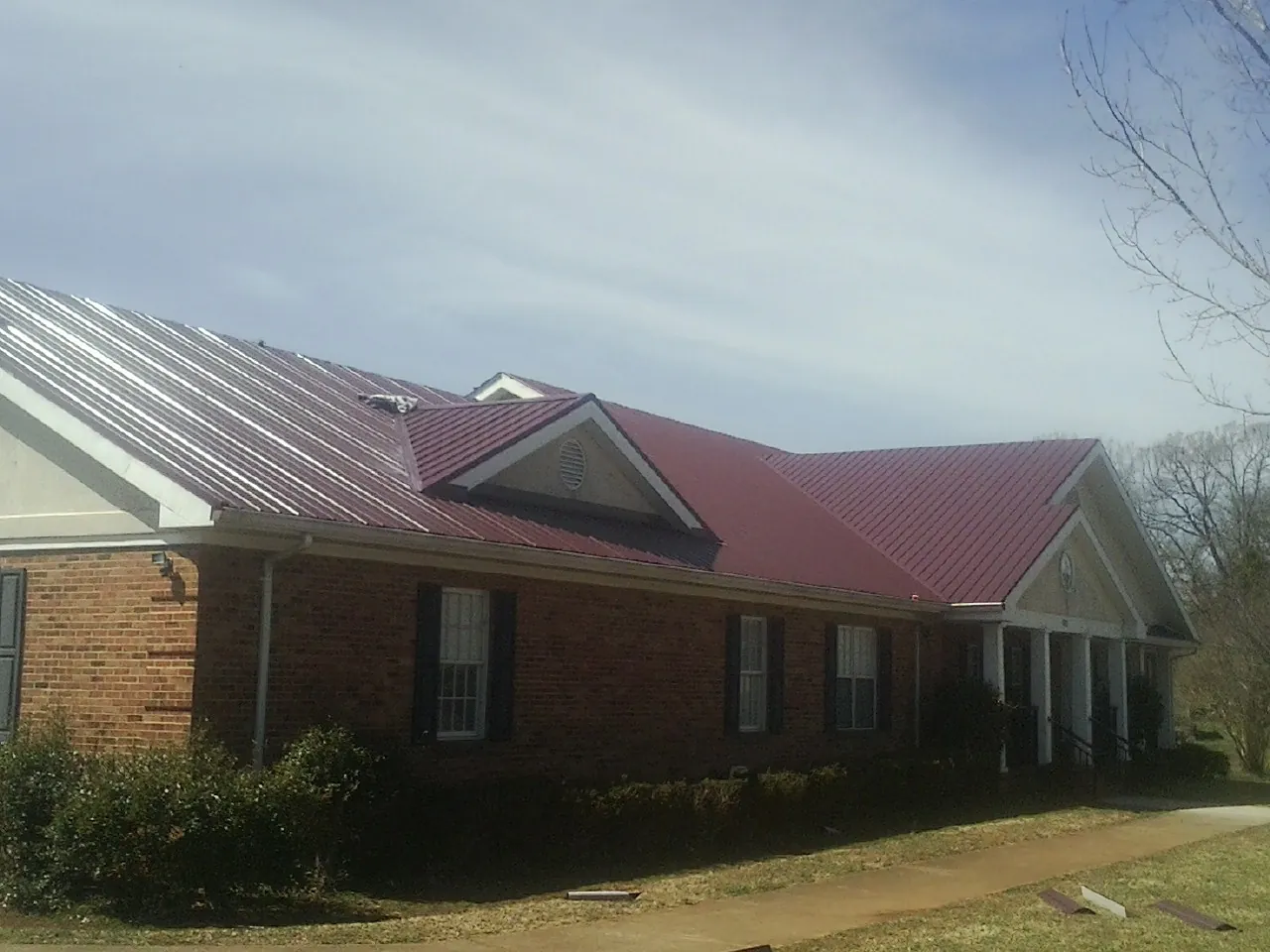 Red metal roof with gabled entries on a long brick building, from a Hail Damage Roof Repair job in Willow Spring