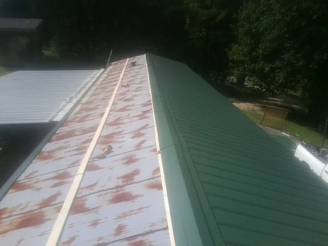 Old rusted panels beside newly installed green metal roofing — Wind Damage Roof Repair by Roofing Brothers in Willow Spring
