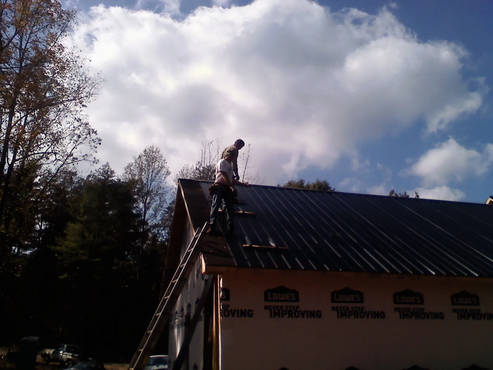 Roofer fastening dark metal panels high against a cloudy sky, from a Roof Inspection job in Willow Spring