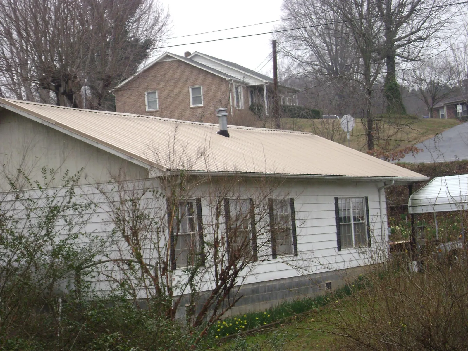 Tan metal roof on a white sided house set into a hillside — Commercial Roofing by Roofing Brothers in Willow Spring