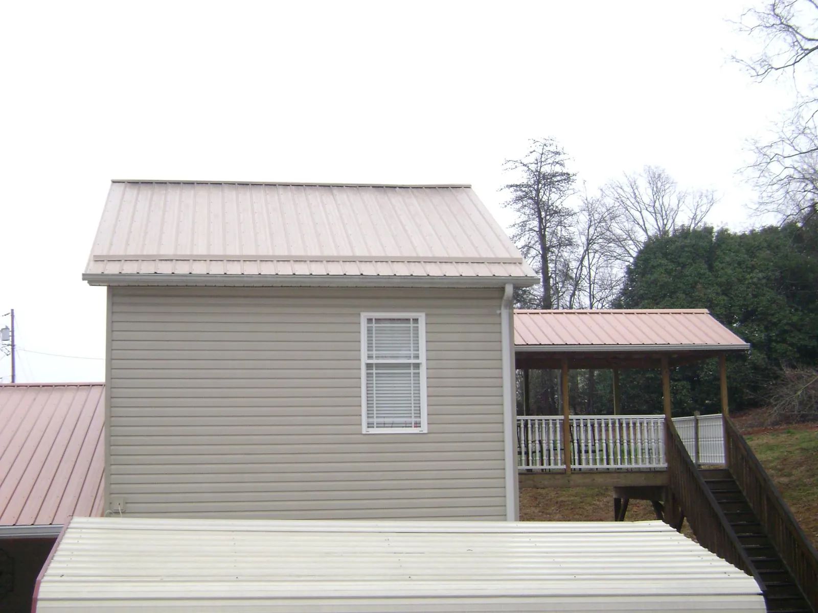 Tan metal roofs on a two story addition and attached porch, from a Roof Replacement job in Willow Spring